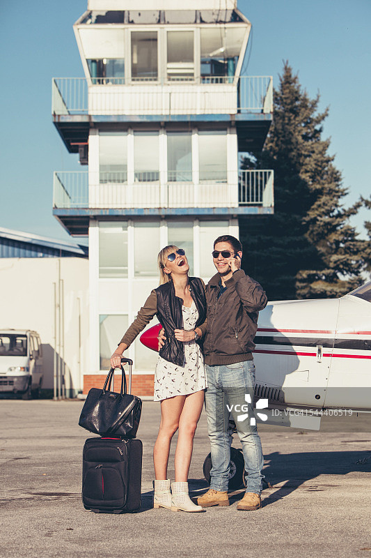 年轻夫妇带着行李乘螺旋桨飞机，男人在用手机图片素材