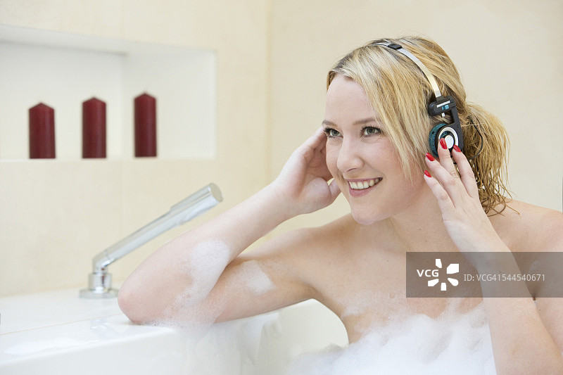 在浴缸里戴着耳机的金发年轻女人图片素材