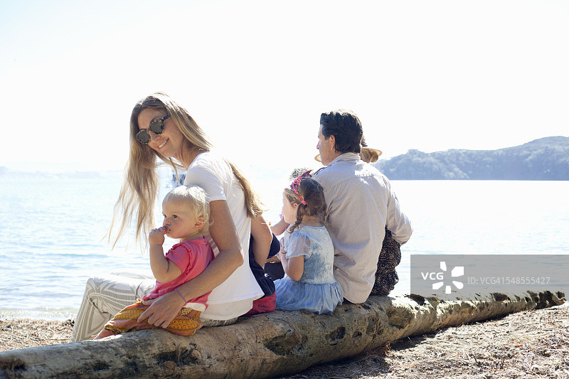 家人和朋友坐在新西兰海滩的树干上图片素材