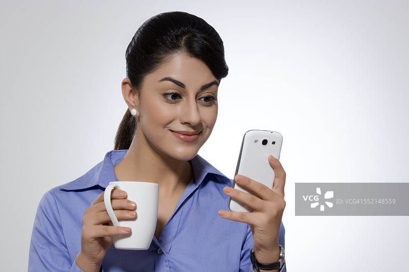 女商人拿着咖啡杯微笑着在灰色背景下看智能手机上的短信图片素材