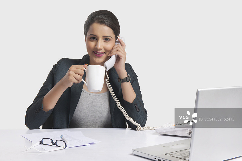 女商人在白色背景下的办公桌边喝咖啡边接电话的肖像图片素材