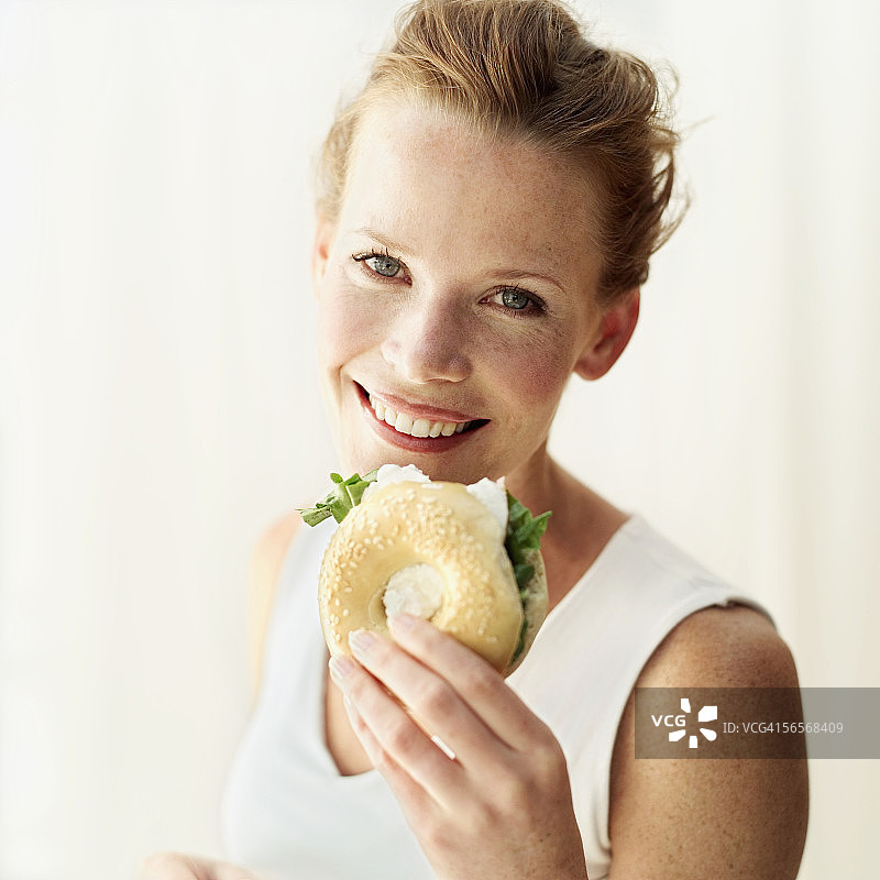 一个年轻女人拿着百吉饼三明治的肖像图片素材