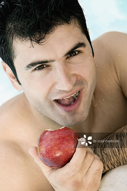 一个年轻人在游泳池里吃苹果的肖像图片素材