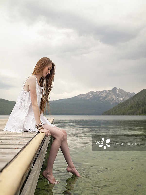 一个少女坐在山湖边的码头上图片素材