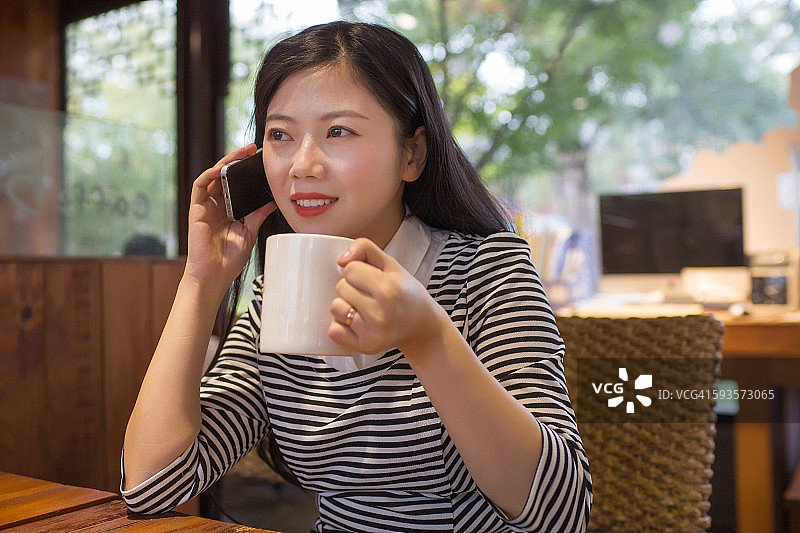 一个年轻的亚洲女人在咖啡馆里用手机图片素材
