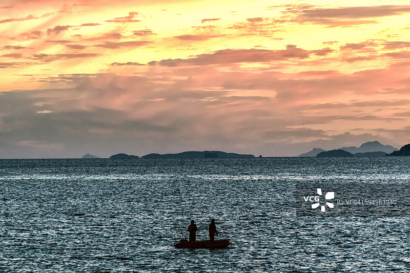 两个人在夕阳下的海面上钓鱼图片素材