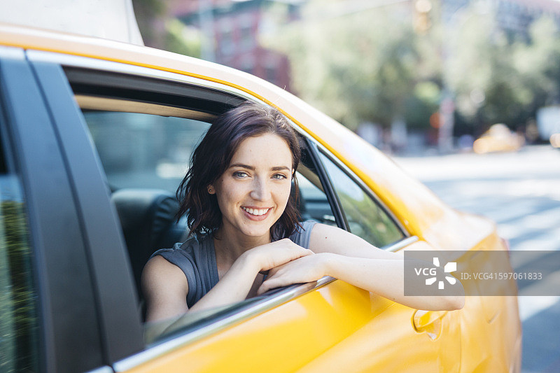 美国，纽约市，一名微笑的年轻女子坐在黄色出租车里图片素材