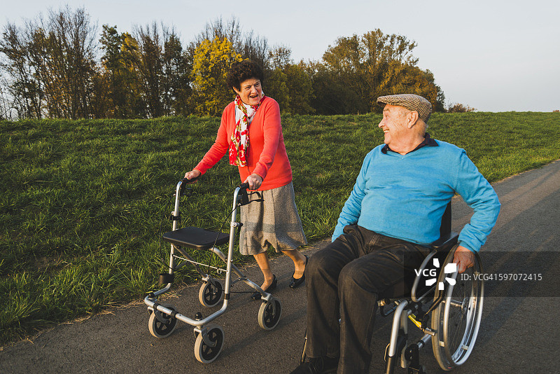 微笑的老夫妇与轮椅和轮式步行者在一条小路上图片素材