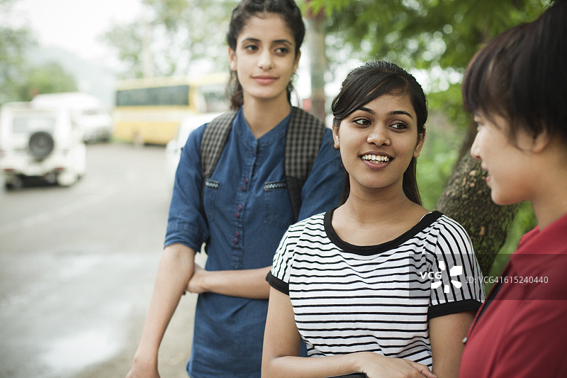 女学生在路边等公共汽车时闲聊。图片素材