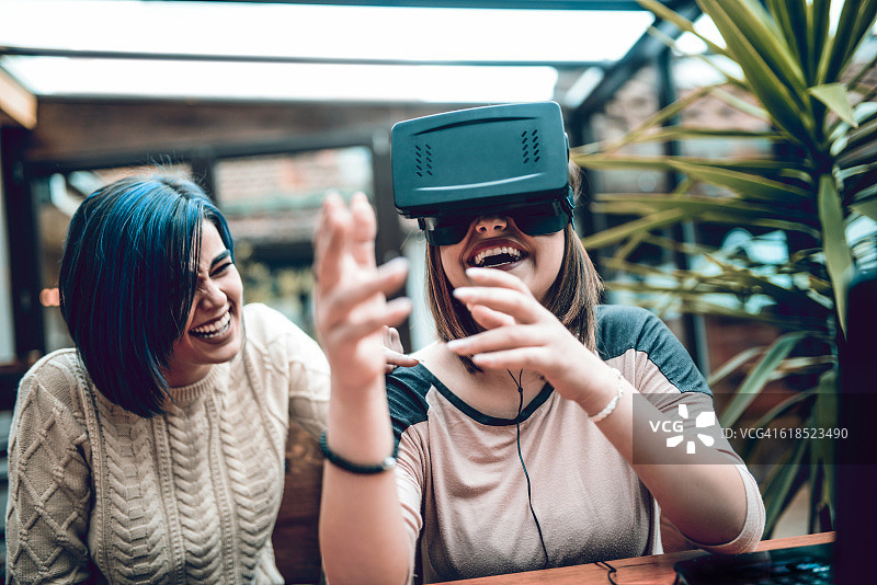 两个女孩在咖啡馆玩虚拟现实模拟器图片素材