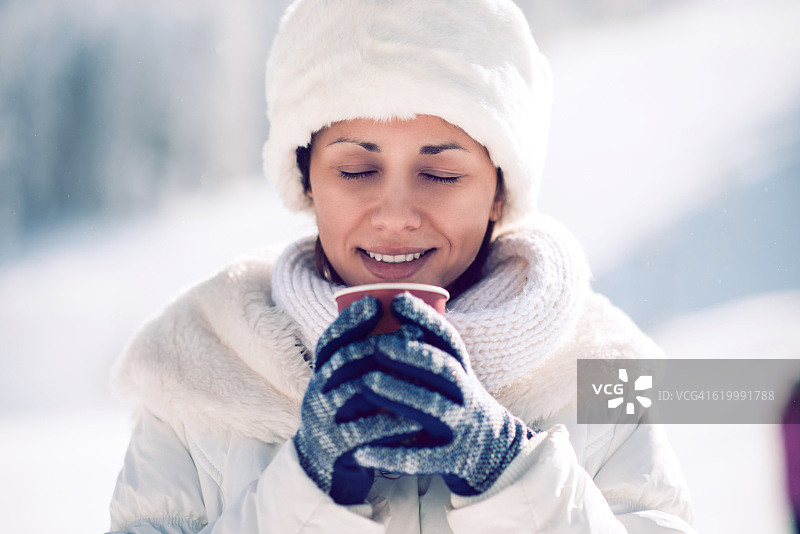在冬天的雪地里，一个年轻女人拿着热饮料杯图片素材