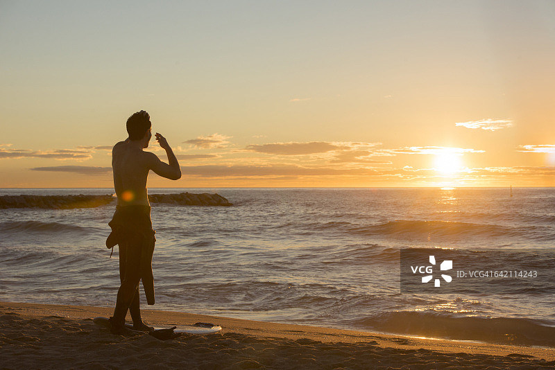 冲浪者站在海滩上看日出的背影图片素材