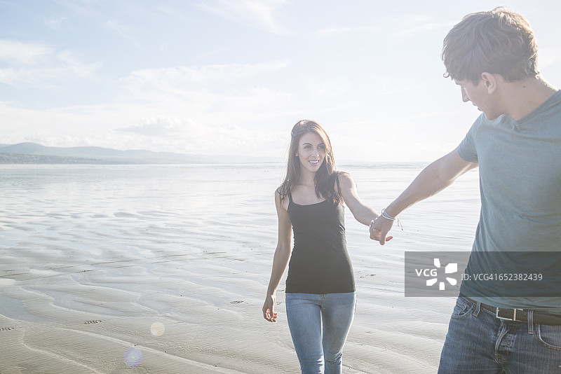 一对年轻夫妇手牵着手走过波特马多克的海滩图片素材