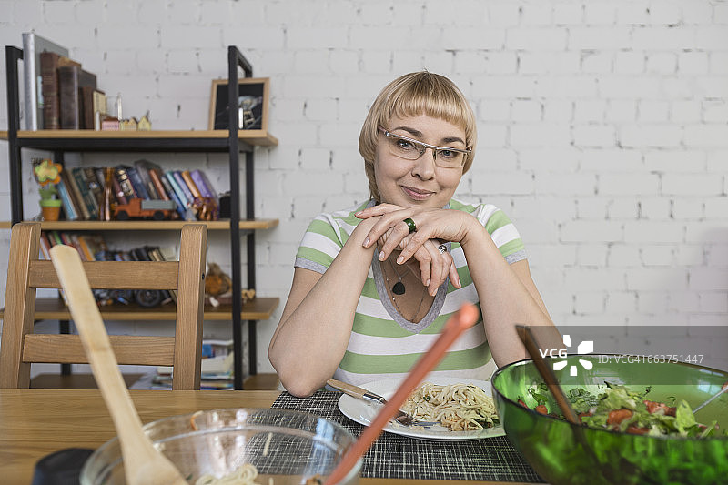 微笑的女人坐在桌子上吃意大利面的肖像图片素材