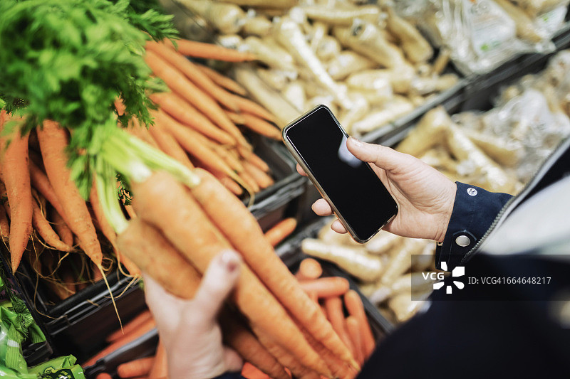 在超市买胡萝卜的时候用手机的女人图片素材