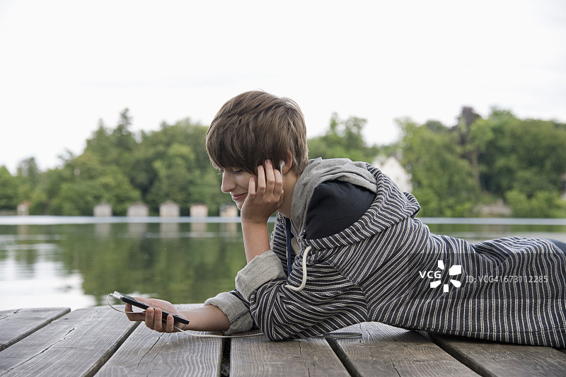 十几岁的女孩躺在湖边的木板路上，戴着耳机听音乐图片素材