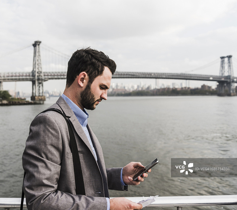 美国，纽约市，商人在东河的渡轮上查看手机图片素材