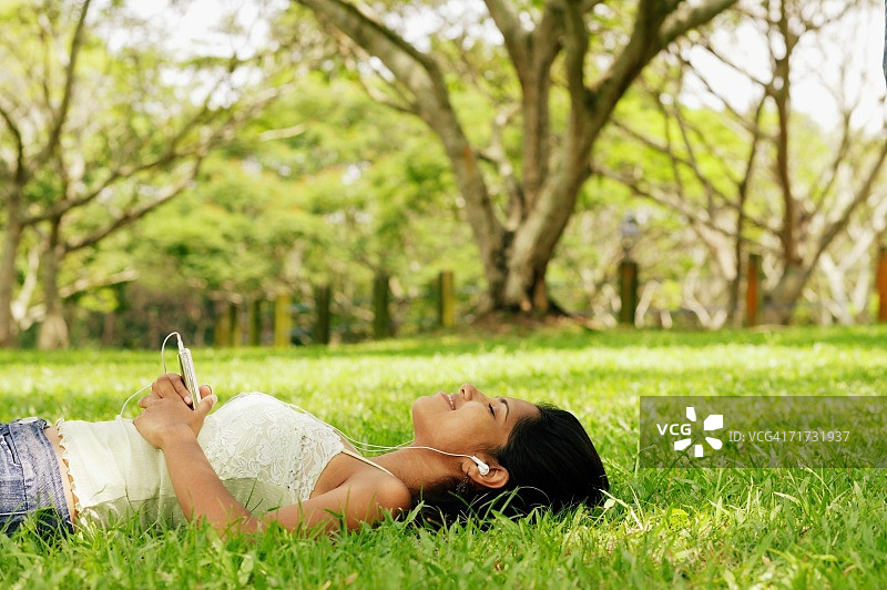 年轻女子躺在草地上，戴着耳机图片素材
