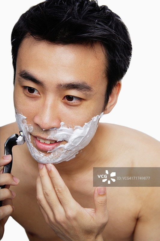 男人拿着剃须刀，刮着脸图片素材