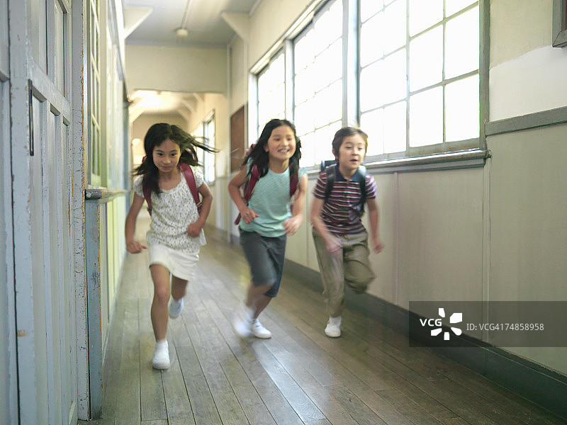 三个孩子(7-9岁)在学校走廊上奔跑图片素材