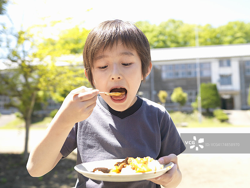 男孩(6-7岁)在学校操场上吃咖喱图片素材