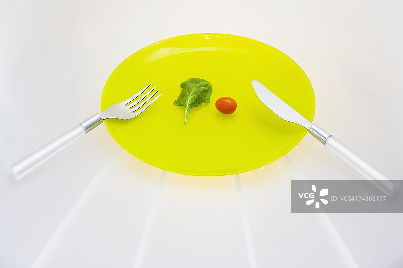 一张叉子和刀的特写，盘子上有一个樱桃番茄图片素材
