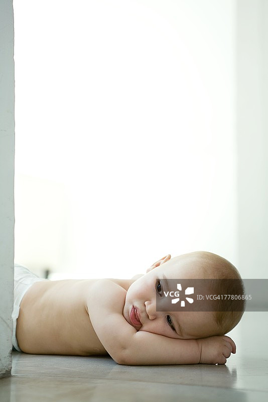 婴儿躺在地板上，头枕在胳膊上图片素材