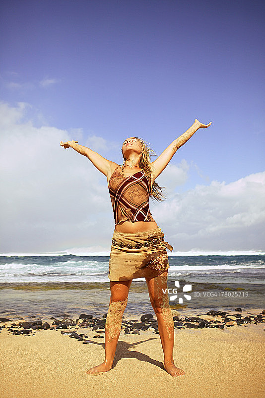 一个女人站在海滩上，她的双臂伸向天空。图片素材