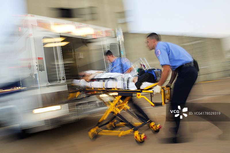 两名医护人员用担架将一名病人抬到一辆救护车的后面，动态使图像变得模糊图片素材