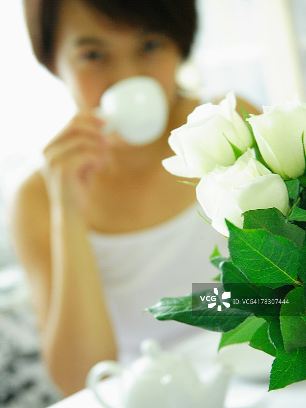 一个花瓶的特写，背景是一个年轻女子在喝茶图片素材