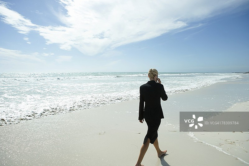 女商人用手机，赤脚走过海滩，全身，后视镜图片素材