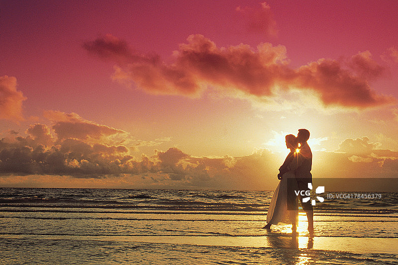 一对情侣在日落时在海滩上摆姿势图片素材