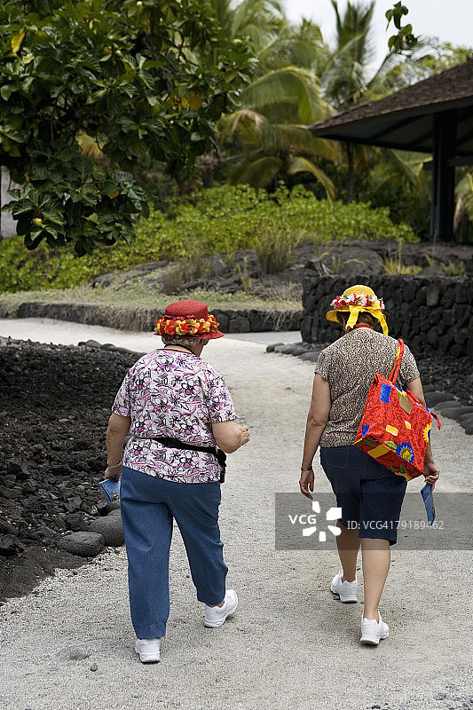 两名妇女走在人行道上的后视图，普乌霍纳奥霍纳瑙国家历史公园，科纳海岸，大岛，夏威夷群岛，美国图片素材
