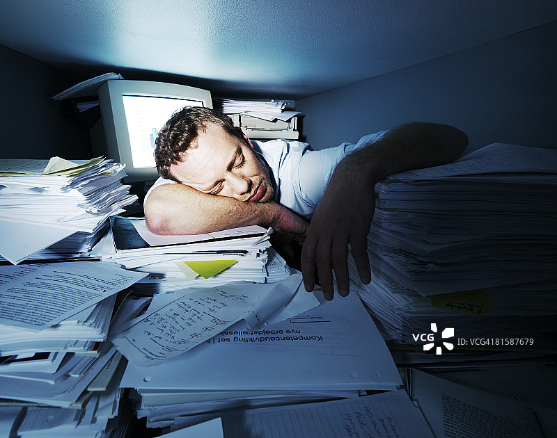 一个人睡在一堆工作在一个非常小的办公室。图片素材