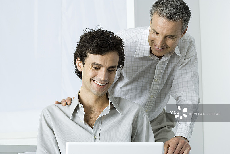 父亲和成年的儿子一起使用笔记本电脑，两人都面带微笑图片素材
