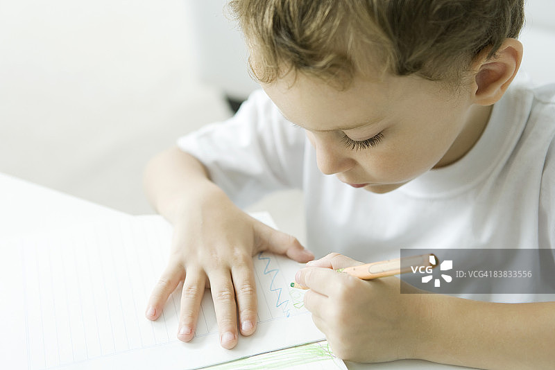 小男孩坐在桌子旁，用彩色铅笔画画图片素材