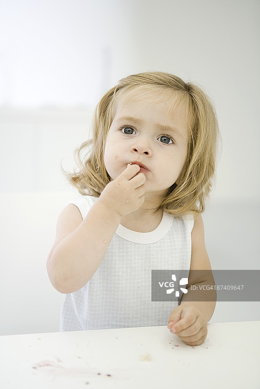 小女孩坐在凌乱的桌子旁，擦着嘴唇上的面包屑图片素材