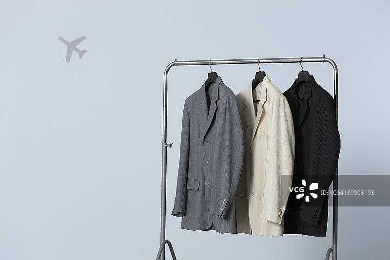衣架上挂着三件男士西装外套，背景是飞机形状图片素材