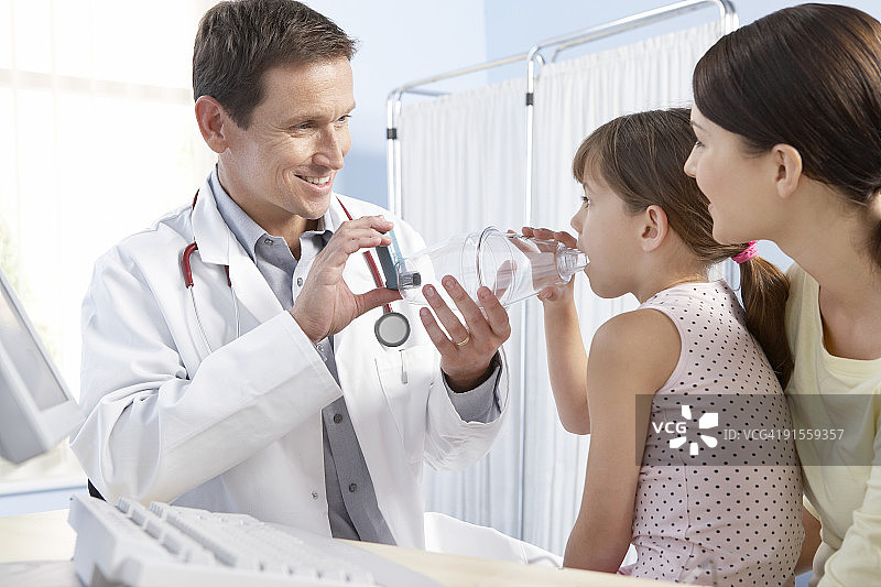 医生帮助年轻女孩使用带吸入器(蓝色)的间隔器(塑料室)治疗哮喘图片素材