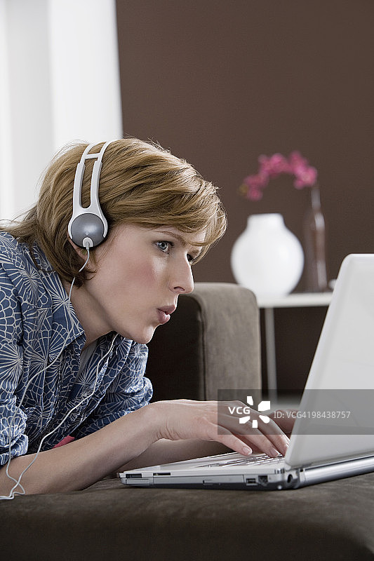 年轻女子在家里戴着耳机与笔记本电脑工作图片素材
