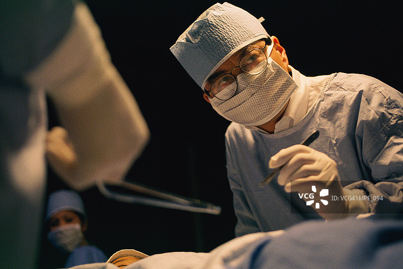 外科医生拿着手术刀，俯身看着病人图片素材