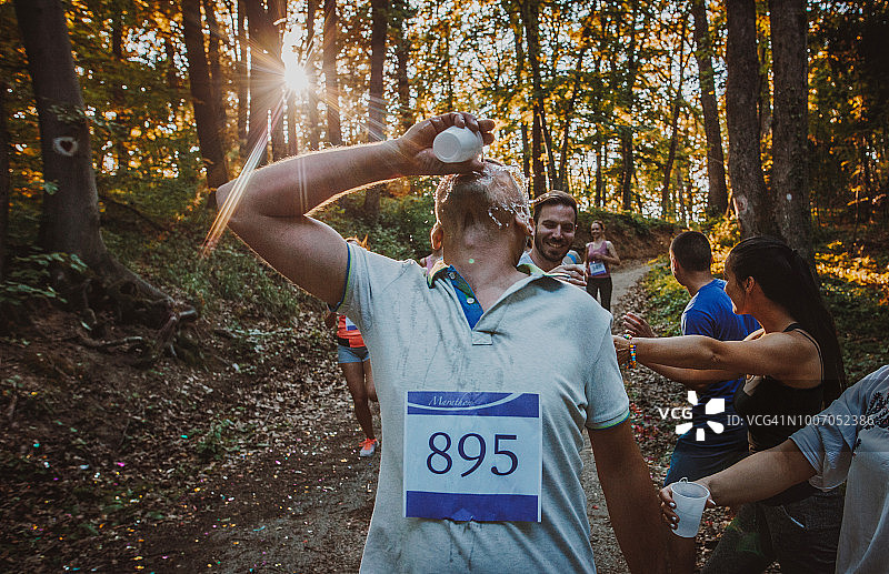 在森林里参加马拉松比赛时，口渴的男子把水倒在自己身上。图片素材