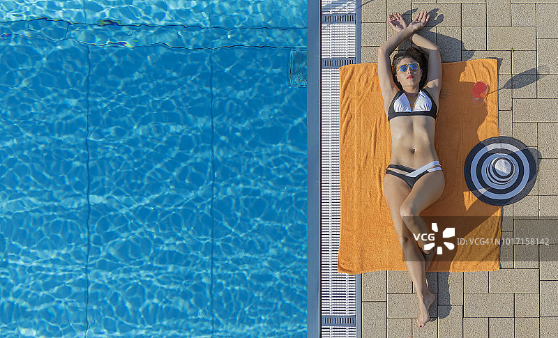 美丽的年轻女子日光浴在比基尼附近的游泳池图片素材