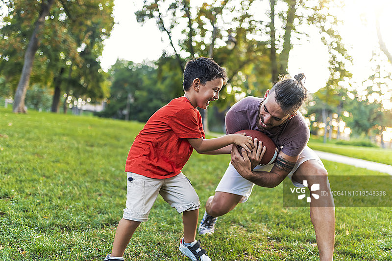 快乐的男孩和父亲在公园玩橄榄球图片素材