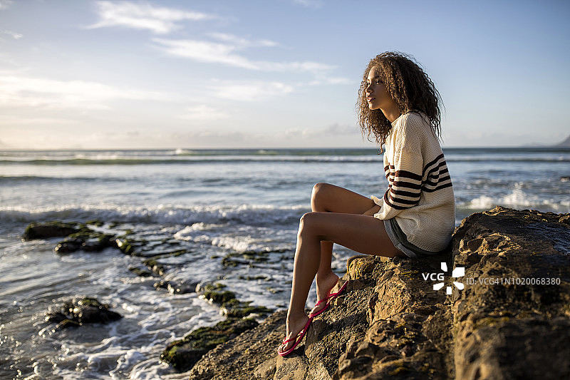 年轻女子坐在海边的岩石上看风景图片素材