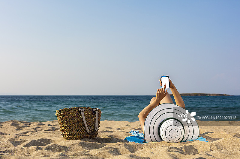 在海滩上拿着智能手机的女人图片素材