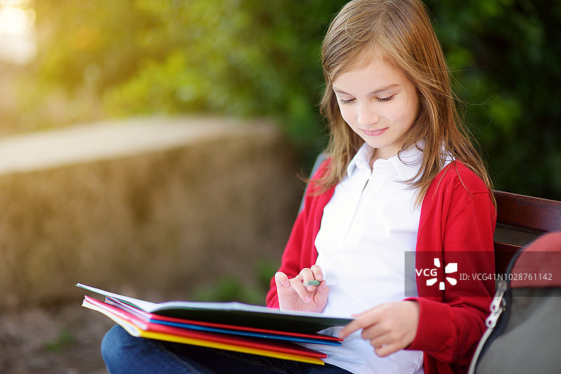 可爱的小女孩在晴朗的秋日在户外学习。年轻的学生在做她的家庭作业。对小孩子的教育。图片素材