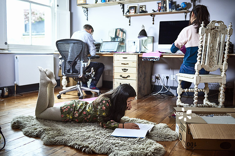 十来岁的女孩在学校放假时躺在父母的家庭办公室里看书图片素材
