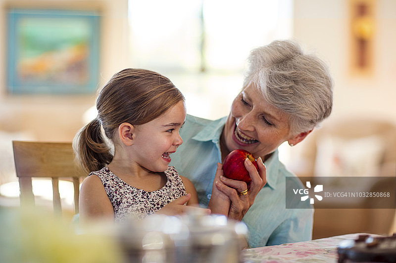 孙女坐在奶奶膝上，手里拿着一个苹果图片素材