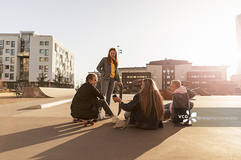 朋友看青少年展示手机的女孩坐在滑板上的城市图片素材